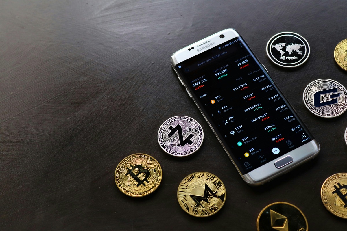 smart phone surrounded by cryptocurrency coins on a table. The smartphone screen displays a beginner's asset portfolio in a cryptocurrency wallet.